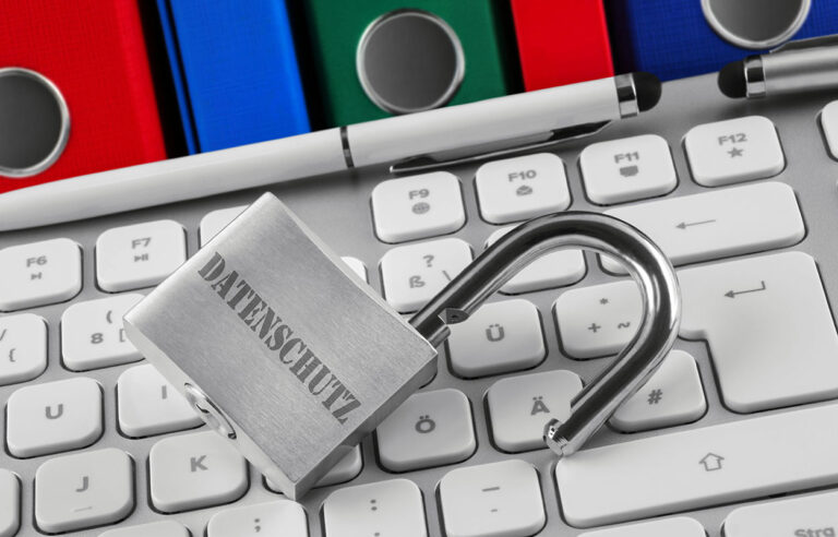 Fallstricke des revidierten Datenschutzgesetzes. Das Bild zeigt ein Vorhängeschloss mit der Aufschrift Datenschutz, auf einer Tastatur liegend. Im Hintergrund sind Ordner zu sehen.