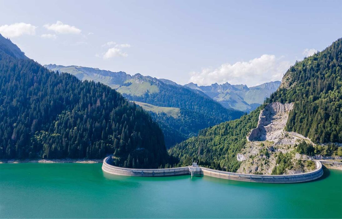 Strommangellage: einzig kurzfristige Entwarnung. Bild zeigt einen Staudamm in den Schweizer Voralpen mit zur Zeit hohem Wasserstand. Das strukturelle Problem der Schweiz bleibt für die kommenden Jahre bestehen und kann angebotsseitig nicht kurzfristig behoben werden. Deshalb sind die Unternehmen gut beraten, sich weiterhin gut und umfassend vorzubereiten.