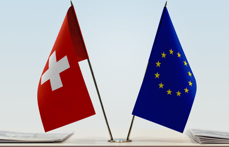 bilaterale_III_Verhandlungsmandat. Das Bild zeigt die Schweizer und EU-Flagge auf einem Tisch mit Dossiermappen, stellvertretend für die Verhandlungen im Rahmen der Bilateralen III.