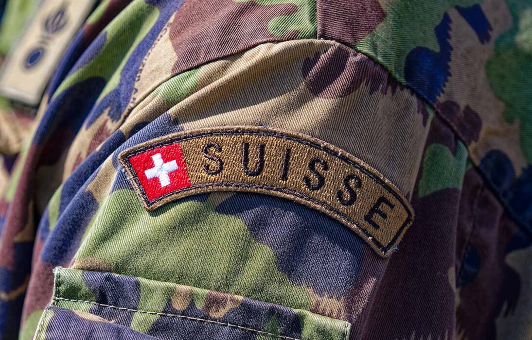 Armee: Glaubwürdigkeit hat ihren Preis. wiederherstellen. Nahaufnahme eines Schweizer Soldaten, der mit der Schulter zur Kamera steht mit Fokus auf das Schweizer Kreuz mit dem Schriftzug "Suisse".